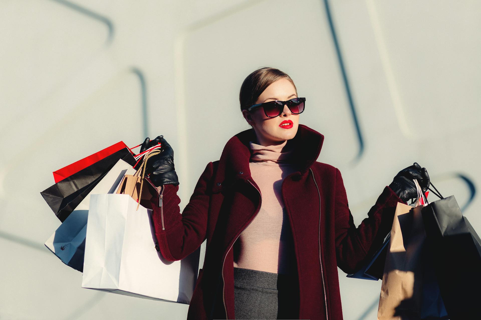Woman in a red coat holding shopping bags against a light background